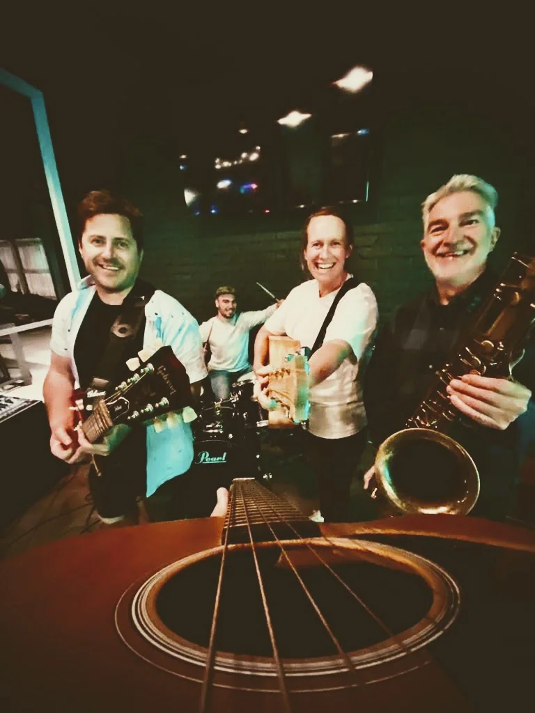 Picture of the band together on stage with a guitar in close up focus